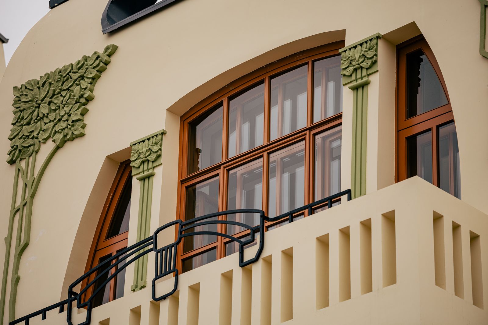 Balcone con ringhiera in ferro e serramenti in legno, decorazioni floreali in stile liberty sulla facciata