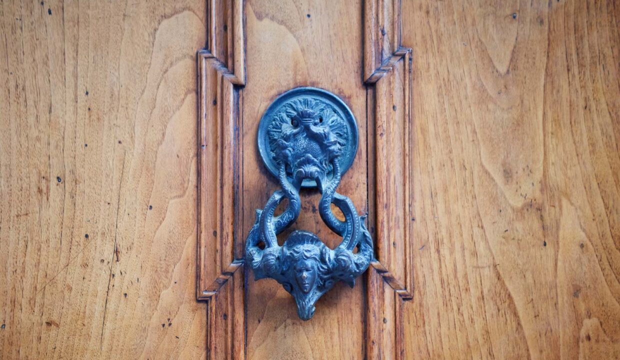 Vecchio antico bussatore di porte vittoriane in metallo sulla porta di legno della vecchia dimora italiana