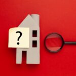 casetta-di-legno-e-punto-interrogativo-su-uno-sfondo-rosso