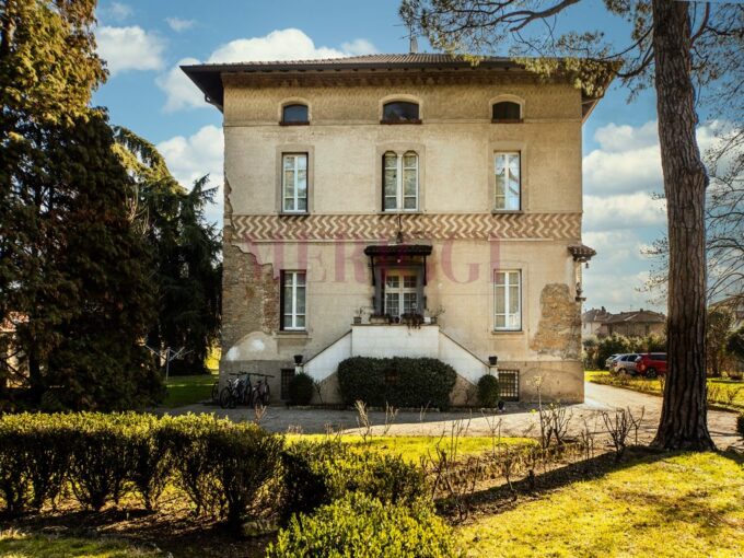 Facciata della villa con scala centrale, balcone e alberi davanti all'ingresso